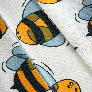 Close-up of fabric material with cute cartoon bee patterns and fine mesh texture