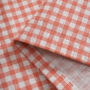 Close-up of orange and white gingham fabric showing fine linen texture and hemmed edges