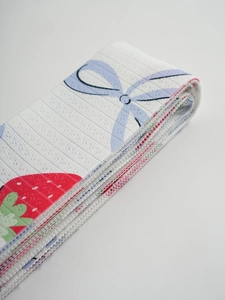 Detail of white fabric curtain band featuring blue bows and red strawberry prints