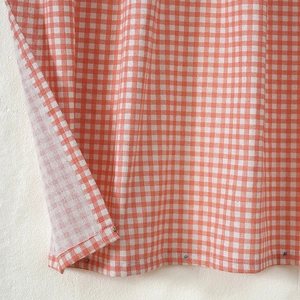 Detailed close-up of orange and white gingham cotton linen fabric with refined stitching
