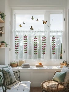 Close-up of white sheer cafe curtain with green leaf embroidery and pom-pom trim