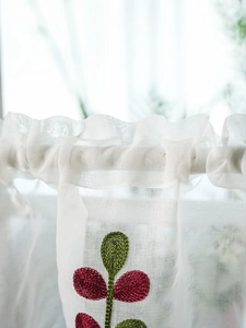 Detail of white sheer curtain featuring textured red leaf embroidery and ruffled top