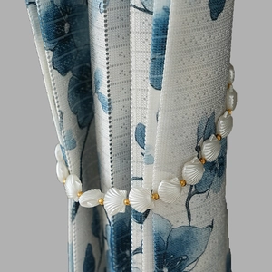 Elegant white shell bead curtain tieback with gold accents on a floral curtain