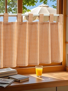 Detail of orange and white checkered cafe curtain with tab top hanging on a wooden window