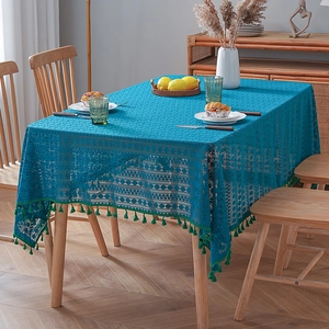 Peacock blue lace tablecloth with hollow patterns and green tassels on wooden dining table