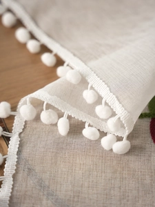 Detail of sheer white curtain with leaf embroidery and decorative pom-pom fringe trim