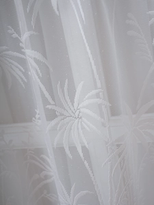 Close-up of white lace curtain fabric featuring intricate tropical palm leaf patterns