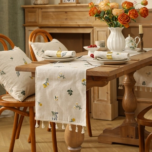 Close-up of linen table runner with floral embroidery and white tassel fringe detailing