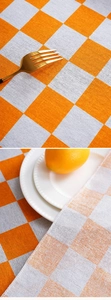 Close-up of orange checkerboard tablecloth fabric showing weave texture and durable hemmed edges
