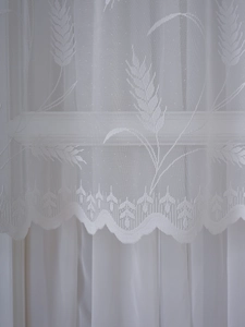 Macro detail of white lace kitchen curtain showing wheat patterns and mesh texture