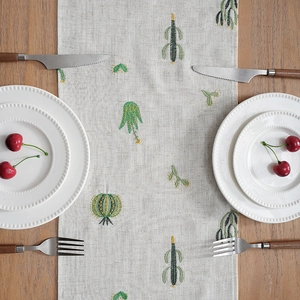 Linen table runner with cactus embroidery on rustic wood surface with tableware
