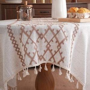 Thick linen tablecloth with geometric embroidery and tassels in a rustic dining setting