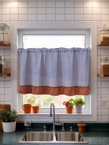 Detail of blue plaid cafe curtain with ruffled hem on a sunny kitchen window