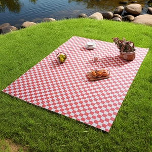 Classic red and white checkered waterproof picnic mat spread on a lush green lawn