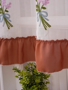 Detail of floral embroidery and caramel ruffled hem on a white sheer cafe curtain