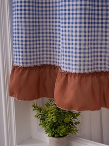 Detail view of a plaid cabinet curtain with coffee brown ruffled hem in a home setting