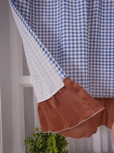 Detail of blue and white checkered cabinet curtain with decorative brown ruffled hem trim