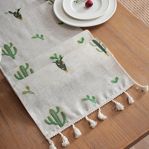 Linen table runner with cactus embroidery and handmade tassels on wooden dining table