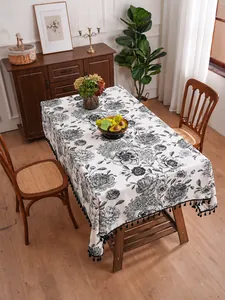 Detail of vintage floral linen tablecloth featuring elegant black tassels on a wooden table