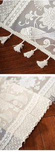 Detailed embroidery of flowers and birds on white lace fabric with tassel edge