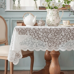 Elegant white lace tablecloth with floral patterns and scalloped edges on a wooden dining table