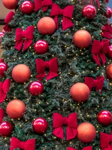Detail of red velvet bow and festive ornaments on Christmas tree with warm LED lights
