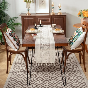Off-white lace table runner with floral embroidery and tassels on a wood table