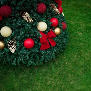 Close-up of red velvet bows and colorful baubles on a Christmas tree against green grass
