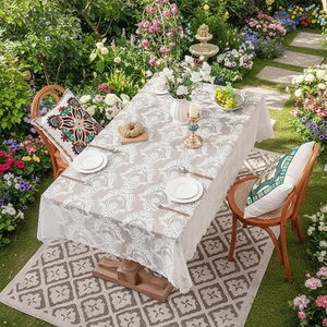 Elegant white lace tablecloth with damask pattern on wooden table in a sunny garden