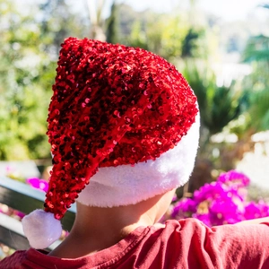 Sparkling red sequin Christmas hat with white plush trim worn by a model outdoors