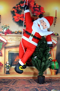 Detail of climbing Santa Claus plush figure on rope with festive fireplace background