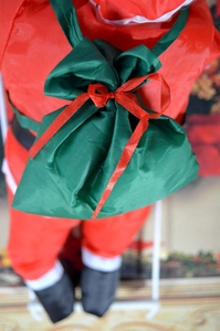 Détail du sac cadeau de Noël vert à cordon avec nœud rouge sur un père Noël en peluche