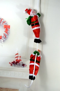 Détail de deux figurines de Père Noël grimpant sur une corde près d'une cheminée de fête