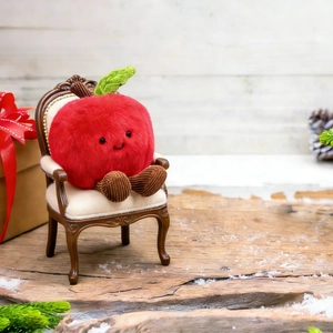 Close-up of a smiling plush apple Christmas ornament sitting on a tiny royal chair