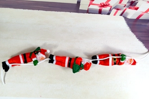 Detailed view of three Santa Claus figures climbing a white rope for Christmas decoration