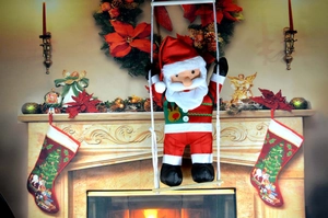 Detail of plush Santa Claus sitting on a wooden swing with fireplace background decor