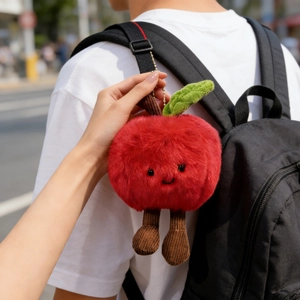 Detailed close-up of a plush red apple charm with corduroy legs hanging on a backpack