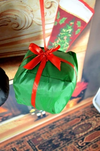 Close-up of a green Christmas gift box ornament with a red ribbon on a festive background