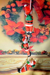 Detailed view of three Santa Claus dolls climbing a white rope for Christmas decor