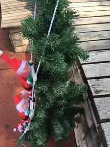 Close-up of two climbing Santa Claus figures on a white ladder hanging on green pine branches