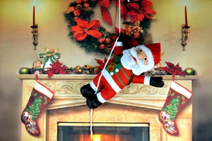 Detail of Santa Claus plush hanging by a fireplace with festive Christmas garlands