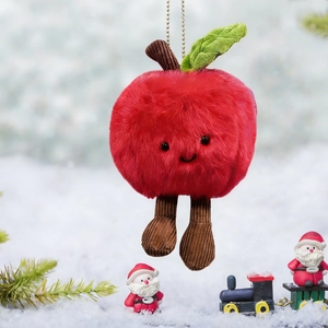 Plush Christmas apple ornament with a smiling face and legs hanging in a snowy outdoor scene