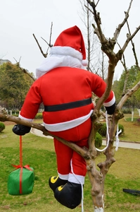 Outdoor climbing Santa Claus decoration with green gift box hanging on a tree trunk