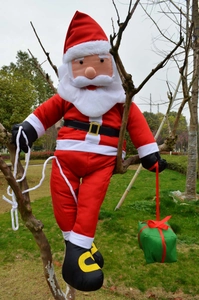 Detail of Santa Claus figure with gift box climbing a rope on an outdoor tree