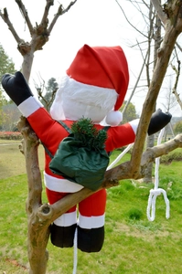 Detail of Santa Claus figure climbing a rope with green gift bag and pine needles