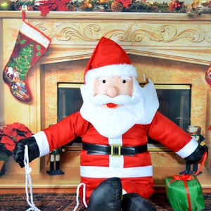 Climbing Santa Claus decoration with gift box hanging by a rope near a festive fireplace