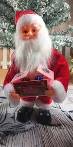 Close-up of Santa Claus doll holding a Merry Christmas gift box with snowy tree background