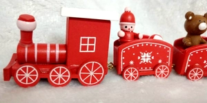 Detail of red wooden Christmas train with santa figures and bear on white plush surface