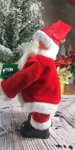 Detail of animated Santa doll in velvet suit holding a green gift box by a Christmas tree