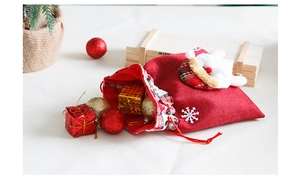 Close-up of red burlap Christmas gift bag with white snowflakes and festive doll decor